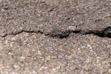 Crack in asphalt, pits and destroyed pavement, selective focus, close-up, perspective.