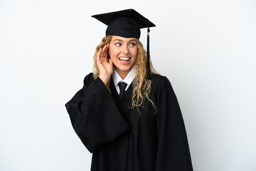 Young university graduate isolated on white background listening to something by putting hand on the ear