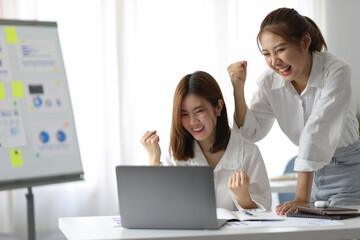 Asian woman and office colleague looking at laptop and showing excited expression.