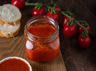 Fototapeta na wymiar Homemade tomato chutney in glass jar on wooden background. Selective focus. Copy space