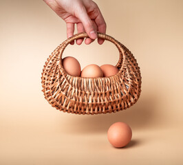 Hand holding basket with farm eggs. Easter celebration tradition or organic food concept on beige background. High quality photo