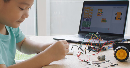 Asia home school young small kid happy smile self study online lesson excited make AI circuit toy. STEM STEAM digital scratch class on laptop screen for active children play arduino enjoy fun hobby.