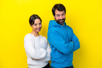 Young caucasian couple isolated on yellow background keeping the arms crossed in lateral position...