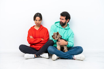 Young caucasian couple sitting on the floor with their pet isolated on white background annoyed angry in furious gesture