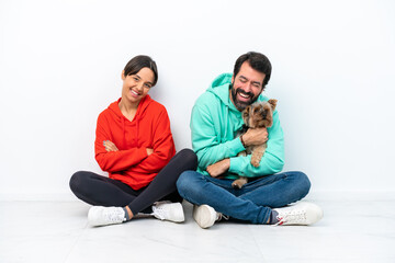 Naklejka na ściany i meble Young caucasian couple sitting on the floor with their pet isolated on white background keeping the arms crossed while smiling