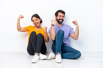 Obraz premium Young caucasian couple sitting on the floor isolated on white background celebrating a victory