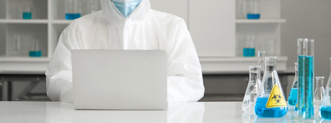 Epidemiological researcher in virus protective cloth typing on laptop computer in laboratory. Omicron strain testing process, Coronavirus disease 2019.