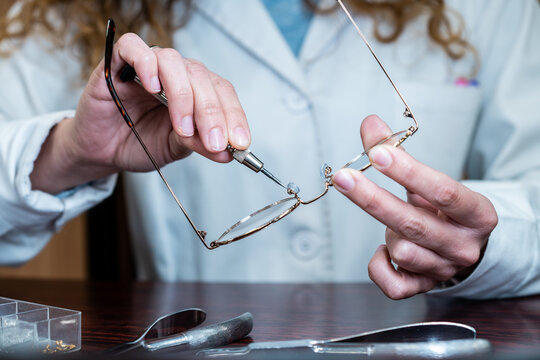 Female optician repairing and fixing eye glasses with screwdriver. Hands holding a mini screwdriver, maintenance and cares service. Frontal view