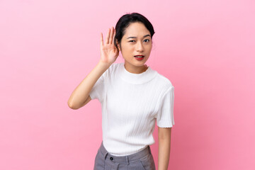 Young Vietnamese woman isolated on pink background listening to something by putting hand on the ear