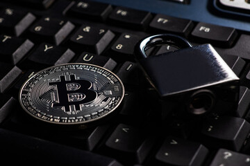 Bitcoin security concept. Silver coin with padlock on computer keyboard.