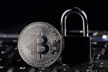 Bitcoin security concept. Silver coin with padlock on computer keyboard.