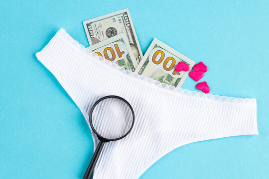 Women's panties with dollar bills, a magnifying glass and hearts on a blue background. The concept of looking for sex for money. High quality photo