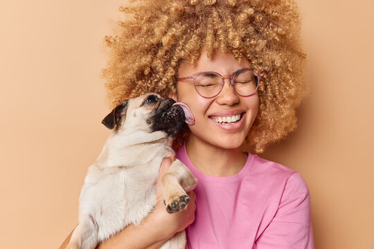 Happy woman gets kiss from favorite pet smiles gladully keeps eyes closed from pleasure. Pug dog licks owner expresses love. People domestic animals responsibility and relatioonship concept. - Powered by Adobe