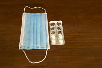 A blue cloth mask and an open blister with large round pills for the treatment and recovery from the pandemic on a brown wooden table