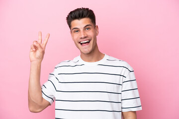 Young caucasian man isolated on pink background smiling and showing victory sign