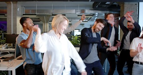Young mixed-races men and women dancing and having fun in office space. Friday after work. Multiethnic team of coworkers having party at work. Cheerful males and females.