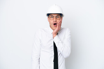 Young architect caucasian man with helmet and holding blueprints isolated on white background with surprise and shocked facial expression
