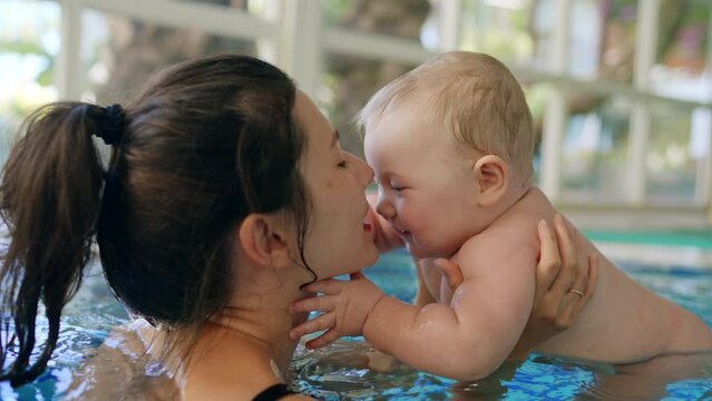 Happy mother with baby son surfing water with fun in swimming pool. Healthy lifestyle, active parent, swimming lessons in indoor swimming pool with child, little fun kid on vacation relax at swim pool