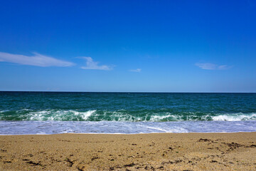 Daytime beach view of rough sea and clear cloudless sky.