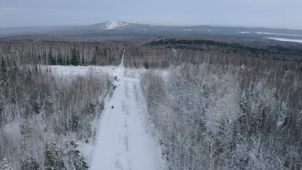 Aerial view of winter landscape with the snow covered field and trees in countryside region. Clip. White road with a driving snowmobile.