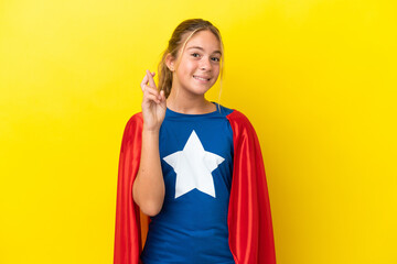 Super Hero little girl isolated on yellow background with fingers crossing and wishing the best