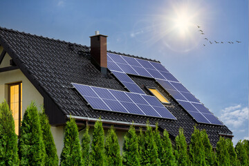 Modern house with solar panels on roof. Photovoltaic panels on roof. Light in windows, green energy...
