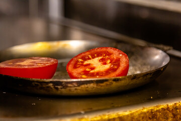 Tomato halves are fried in a steel frying pan