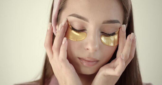 Woman applying hydrogel under-eye recovery patches on a light background