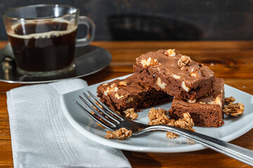 Homemade chocolate brownie squares with pecan pieces served on a white plate. Natural, healthy food concept.