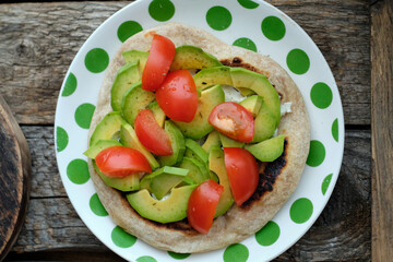 Flatbread with avocado and tomato. Wooden background, top view