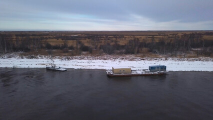 View from a helicopter.Clip. A spring landscape where large ships export cargo along the river next to bare slightly snowy forests.