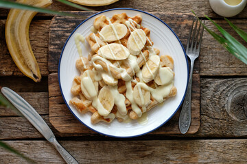 Waffles with banana and white chocolate. Wooden background. Top view. 