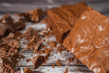 Chocolate brownies on a rustic wooden table with chocolate chips and chocolate soil next to the brownie portions.Close up.