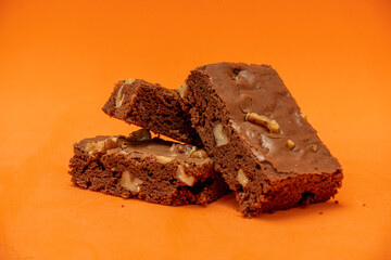 Homemade chocolate brownie squares with pecan pieces. Orange Background. Natural, healthy food concept.