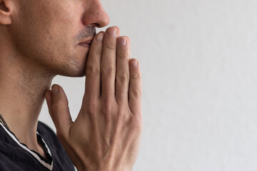 Man praying. Concentrated young man in white shirt holding hands clasped near face while standing against grey background