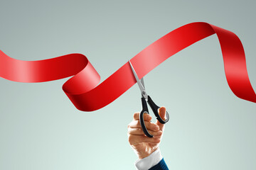 Grand opening with red ribbon and scissors. A businessman's hand holds scissors cuts a red ribbon on a light background. Close-up, copy space. - obrazy, fototapety, plakaty