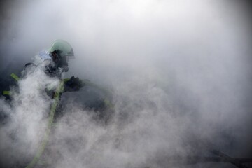 Firefighter with breathing apparatus and hose in thick smoke when extinguishing a fire