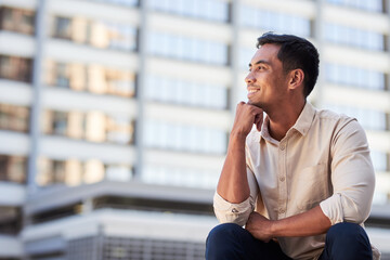 A young Asian businessman sits and looks out over the city smiling