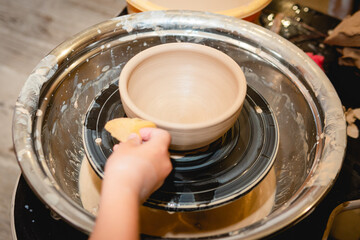 Potter working on potters wheel with clay. Process of making ceramic tableware in pottery workshop. Handicraft and art concept.