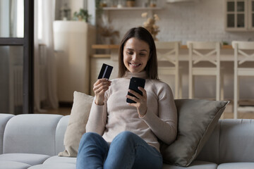 Happy cheerful young customer woman spending money from credit card, enjoying shopping online, paying for purchase on Internet, using ecommerce app on smartphone