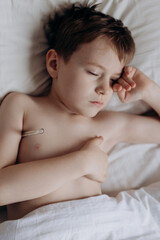 Fototapeta na wymiar sad sick boy with thermometer lying in bed
