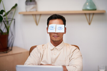 A businessman sleeps at his desk with eyes drawn on stick notes on his face
