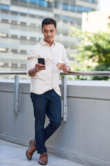 A full body shot of an Asian businessman taking a break on city office balcony