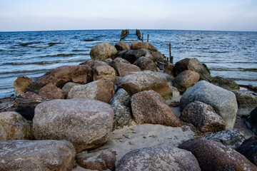 Old wooden poles on the shores of the Baltic Sea with stones in the foreground