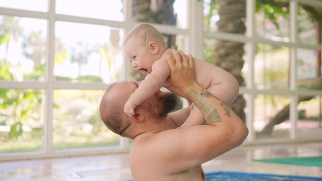 Cute baby having swimming lesson with his mother and father. Healthy family teaching their baby to swim in the swimming pool. Young father takes his son and embraces him while the kid is smiling