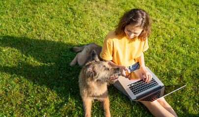 Beautiful happy young woman sitting on the grass with laptop and dog, shot from above