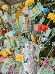 Thai baht and artificial flowers on a Buddhist money tree as gifts. Buddhist culture.