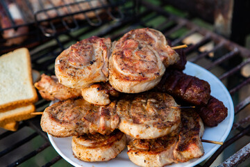 A large variety of grilled meat on the fire outside. Picnic with meat: sausages, pork steak, chicken breast with vegetables. 