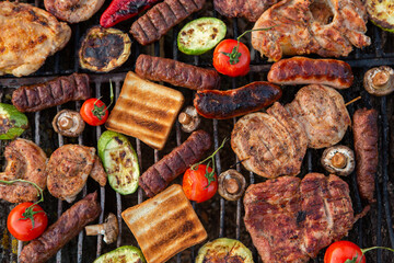 A large variety of grilled meat on the fire outside. Picnic with meat: sausages, pork steak, chicken breast with vegetables. 