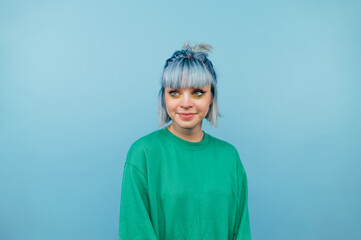 Attractive girl in casual clothes and colored hair stands on a blue background with a smile on his face and looks away.